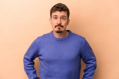 Kafkasyalı genç adam bej arka planda izole, kafası karışmış, şüpheli ve güvensiz hissediyor..