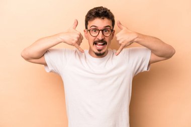 Beyazlı genç bir adam bej arka planda izole edilmiş. Cep telefonu hareketini parmaklarıyla gösteriyor..