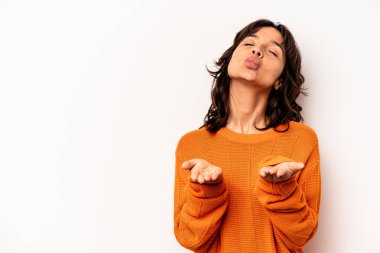 Beyaz arka planda izole edilmiş, dudakları kıvrılmış ve hava öpücüğü yollamak için avuç içi tutan genç İspanyol kadın..