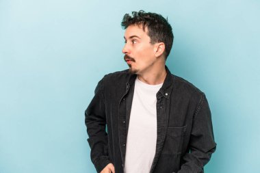 Mavi arka planda soyutlanmış genç beyaz bir adam gülümsüyor, neşeli ve keyifli görünüyor..