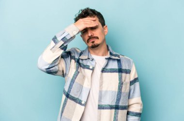 Genç beyaz adam mavi arka planda izole edilmiş tapınaklara dokunuyor ve başı ağrıyor..