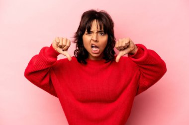 Pembe arka planda izole edilmiş genç İspanyol kadın baş parmağını aşağı gösteriyor ve hoşlanmadığını ifade ediyor..