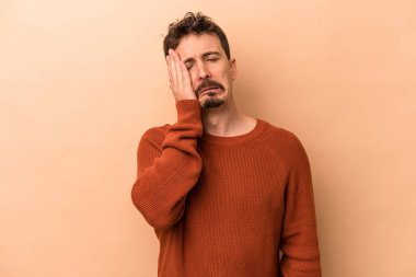 Beyazlı genç bir adam bej arka planda izole edilmiş. Yorgun ve uykulu. Elini başının üstünde tutuyor..