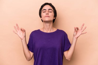 Beyaz tenli genç bir kadın, bej arka planda izole edilmiş yoğun çalışma gününden sonra rahatlıyor, yoga yapıyor..