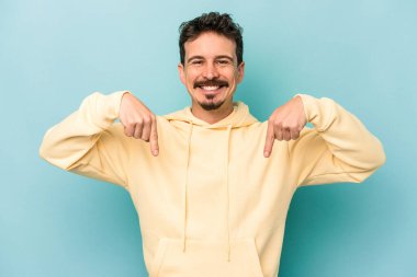 Kafkasyalı genç adam mavi arka planda izole edildi. Parmakları aşağıda, olumlu bir his var..