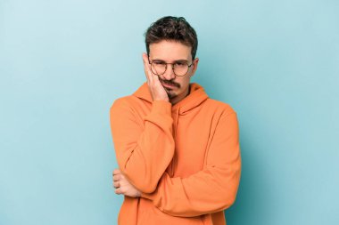 Mavi arka planda izole edilmiş, sıkılmış, yorgun ve dinlenmeye ihtiyacı olan genç beyaz bir adam..