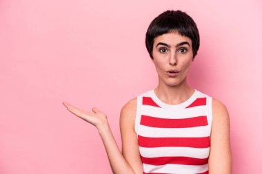 Pembe arka planda izole edilmiş genç beyaz kadın, avuç içi fotokopi alanını elinde tutmaktan etkilenmiş..