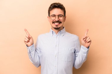 Beyazlı genç bir adam bej arka planda izole edilmiş iki parmağı da boş bir alan gösteriyor..