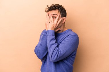 Beyazlı genç bir adam bej arka planda izole edilmiş. Korkmuş ve gergin parmaklarıyla göz kırp..