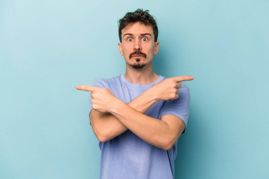 Mavi arka plan noktalarında izole genç beyaz adam, iki seçenek arasında seçim yapmaya çalışıyor.