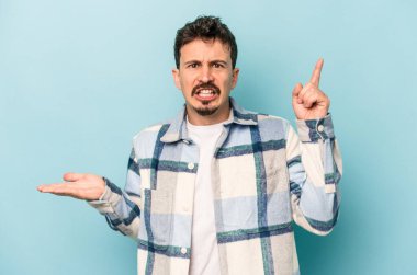 Kafkasyalı genç adam mavi arka planda izole edilmiş ve elinde bir ürün tutuyor..