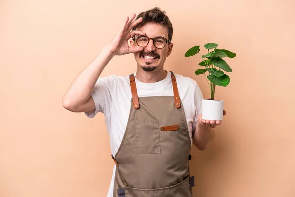 Młody Biały Ogrodnik Człowiek Trzymając Roślina Odizolowany Beżowy Tło Podekscytowany — Zdjęcie stockowe