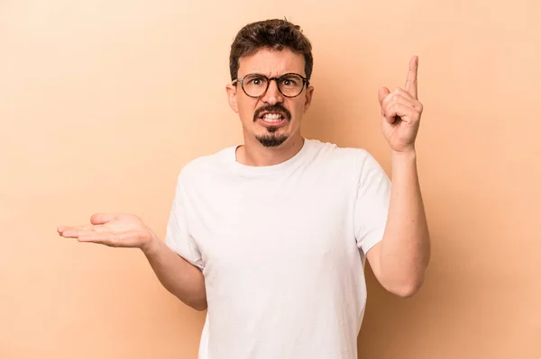 Joven Hombre Caucásico Aislado Sobre Fondo Beige Sosteniendo Mostrando Producto — Foto de Stock