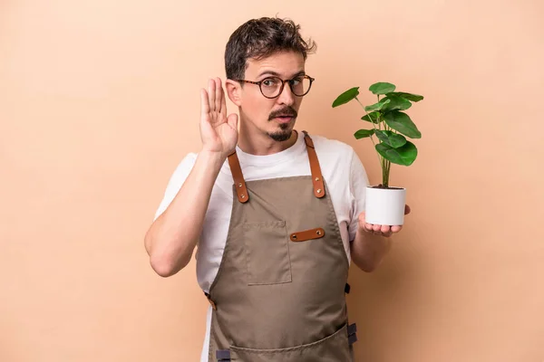 Młody Biały Ogrodnik Człowiek Trzymając Roślinę Odizolowany Beżowym Tle Próbuje — Zdjęcie stockowe