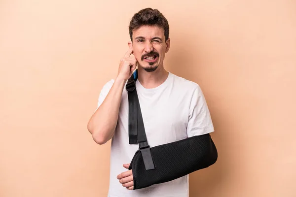Young Caucasian Man Broken Arm Isolated Beige Background Covering Ears — Stock Photo, Image
