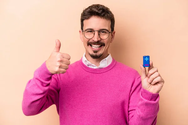 Joven Hombre Caucásico Sosteniendo Baterías Aisladas Sobre Fondo Beige Sonriendo —  Fotos de Stock