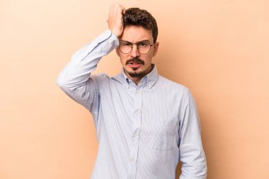 Beyazlı genç bir adam bej arka planda izole edilmiş. Yorgun ve uykulu. Elini başının üstünde tutuyor..