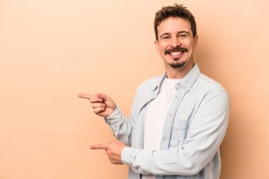 Beyazlı genç adam bej arka planda izole edilmiş. İşaret parmaklarıyla işaret ettiği için heyecanlı..