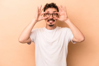 Beyazlı genç bir adam bej arka planda izole edilmiş. Başarı fırsatı bulmak için gözlerini açık tutuyor..