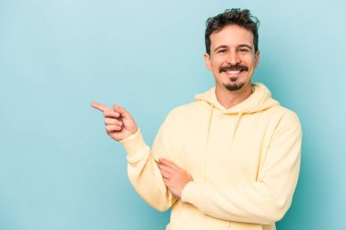 Mavi arka planda izole edilmiş genç beyaz adam işaret parmağıyla işaret ederek gülümsüyor..