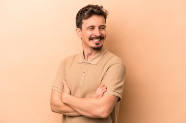 Beyaz tenli genç adam bej arka planda izole edilmiş gülüyor ve eğleniyor..