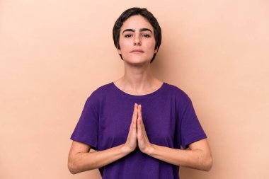 Beyaz tenli genç bir kadın bej arka planda izole edilmiş dua ediyor, bağlılık gösteriyor, dindar biri ilahi ilham arıyor..