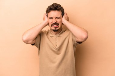 Beyazlı genç bir adam bej arka planda izole edilmiş kulakları elleriyle kapatıyor..