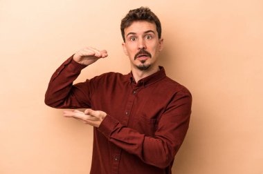 Beyazların arka planında izole edilmiş genç beyaz bir adam iki eliyle bir şey tutuyor, ürün sunumu..