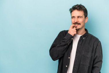 Mavi arka planda izole edilmiş genç beyaz adam rahatlamış bir şeyin fotokopi odasına baktığını düşünüyor..