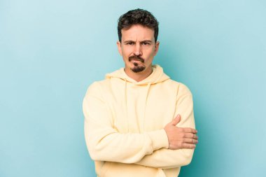 Kafkasyalı genç adam mavi arka planda izole edilmiş hoşnutsuzca kaşlarını çatmış, kollarını kavuşturmuş..