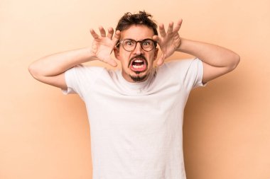 Beyazlı genç bir adam bej arka planda izole edilmiş pençelerini kedi taklidi yaparken gösteriyor, agresif bir hareket..