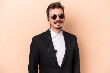 Beyaz tenli genç koruma bej arka planda izole edilmiş gülümsüyor ve keyifli görünüyor..