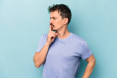 Mavi arka planda izole edilmiş genç beyaz bir adam ya sır saklıyor ya da sessizlik istiyor..