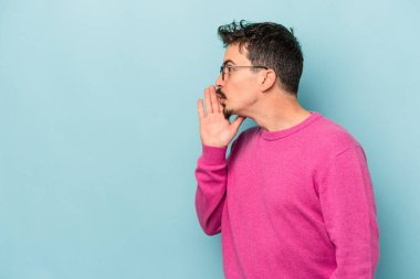 Mavi arka planda izole edilmiş genç beyaz bir adam gizli bir sıcak fren haberi veriyor ve yana bakıyor.