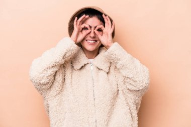 Beyazlı genç bir kadın bej arka planda izole edilmiş, gözlerde sorun yok işareti var.