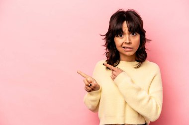 Pembe arka planda izole edilmiş genç İspanyol kadın işaret parmağıyla fotokopi alanını işaret ederek şok oldu..