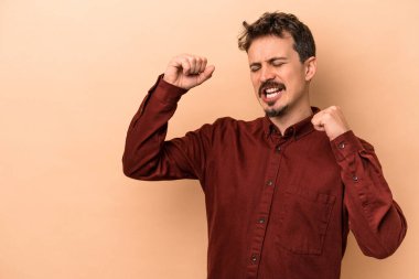 Beyazlı genç adam bej arka planda izole edilmiş zafer kazandıktan sonra yumruğunu kaldırıyor, kazanan konsept.