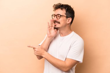 Beyaz tenli genç adam bej arka planda izole edilmiş. Dedikodu yapıyor, bir şeyleri bildiriyor..