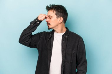 Kafkasyalı genç bir adam mavi arka planda izole edilmiş, başı ağrıyor, yüzüne dokunuyor..