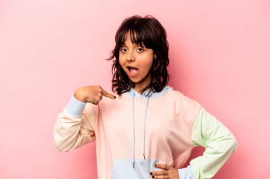 Pembe arka planda izole edilmiş genç İspanyol kadın gömlek fotokopisini elle gösteriyor, gururlu ve kendinden emin.