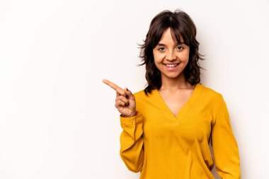 Beyaz arka planda izole edilmiş genç İspanyol kadın işaret parmağıyla işaret ederek gülümsüyor..