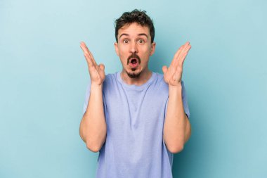 Kafkasyalı genç adam mavi arka planda izole edildi. Şaşırdı ve şok oldu..