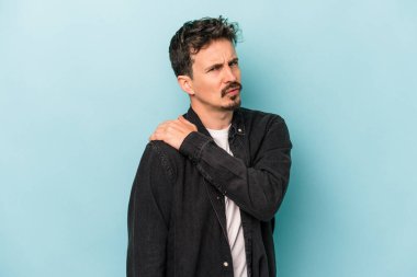 Mavi arka planda izole edilmiş, omuz ağrısı olan genç beyaz bir adam..