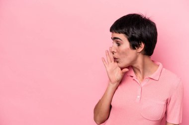 Pembe arka planda izole edilmiş genç beyaz kadın gizli bir sıcak fren haberi veriyor ve yana bakıyor.