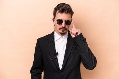 Beyaz tenli genç koruma bej arka planda izole edilmiş. Şakağı parmağıyla işaret ediyor. Düşünüyor, bir göreve odaklanıyor..