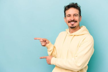 Kafkasyalı genç adam mavi arka planda izole edilmiş. İşaret parmağıyla işaret ettiği için heyecanlı..