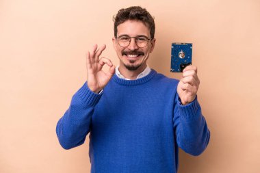 Genç gayri resmi bir adam bej arka planda izole edilmiş neşeli ve kendinden emin, iyi bir jest yapıyor..