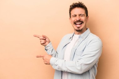 Beyaz tenli genç adam bej arka planda izole edilmiş ve işaret parmağıyla fotokopi alanını işaret ederek heyecan ve arzusunu ifade ediyor..