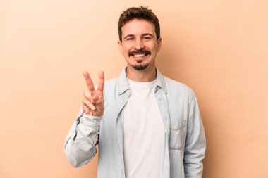 Beyazların arka planında izole edilmiş genç beyaz adam zafer işareti gösteriyor ve gülümsüyor..