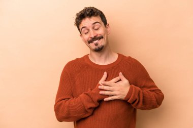 Beyazların arka planında izole edilmiş genç beyaz bir adam dost ifadesine sahip, avuçlarını göğsüne bastırıyor. Aşk konsepti.